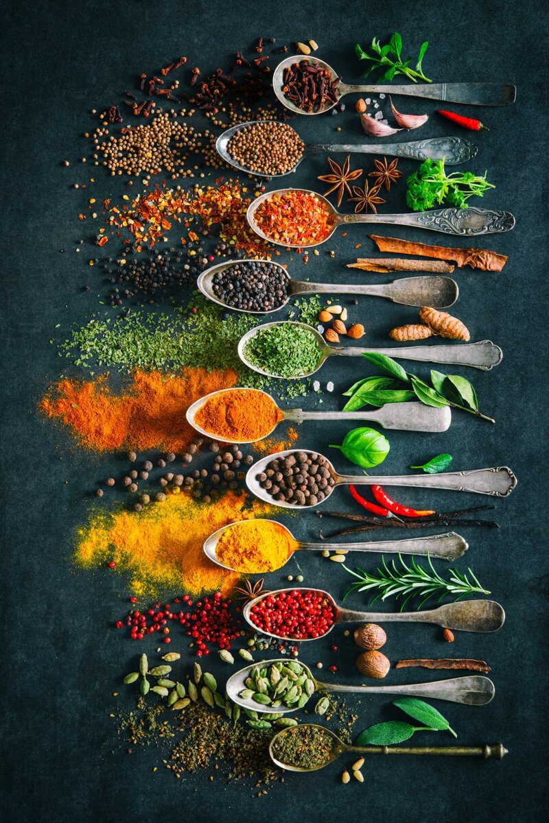Assorted colorful spices and herbs in vintage spoons on dark background, including turmeric, chili, peppercorns, star anise, bay leaves, and cardamom. Culinary spices for cooking, food seasoning, and gourmet recipes.