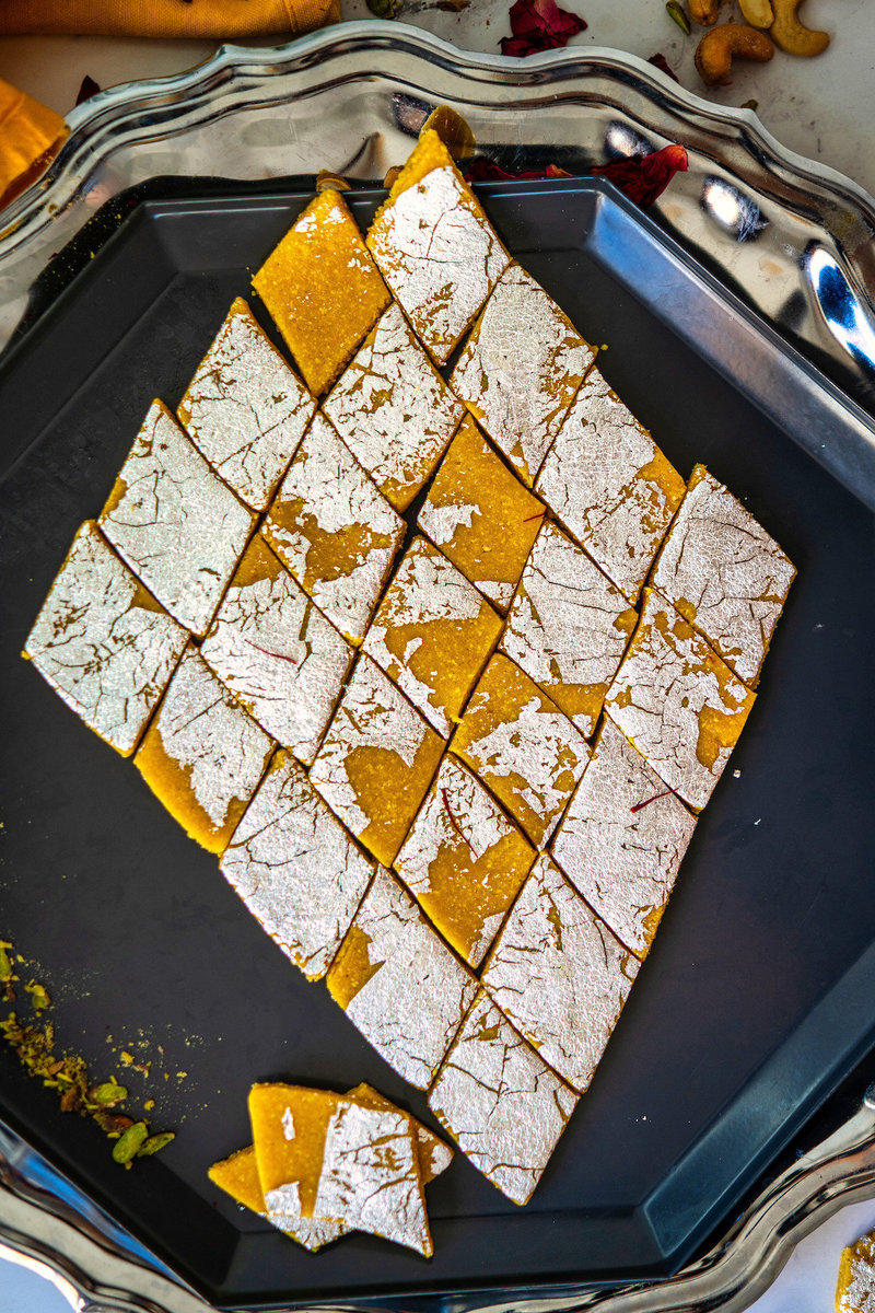 Diamond-shaped kesar kaju katli sweets arranged in a geometric pattern on a dark grey tray.