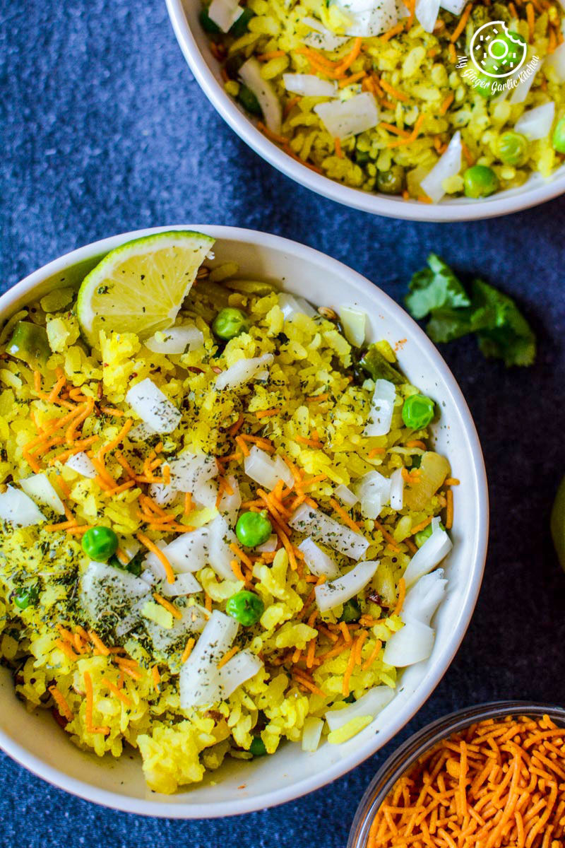 two bowls of khatta meetha indori poha with a topping of sev and cilantro 