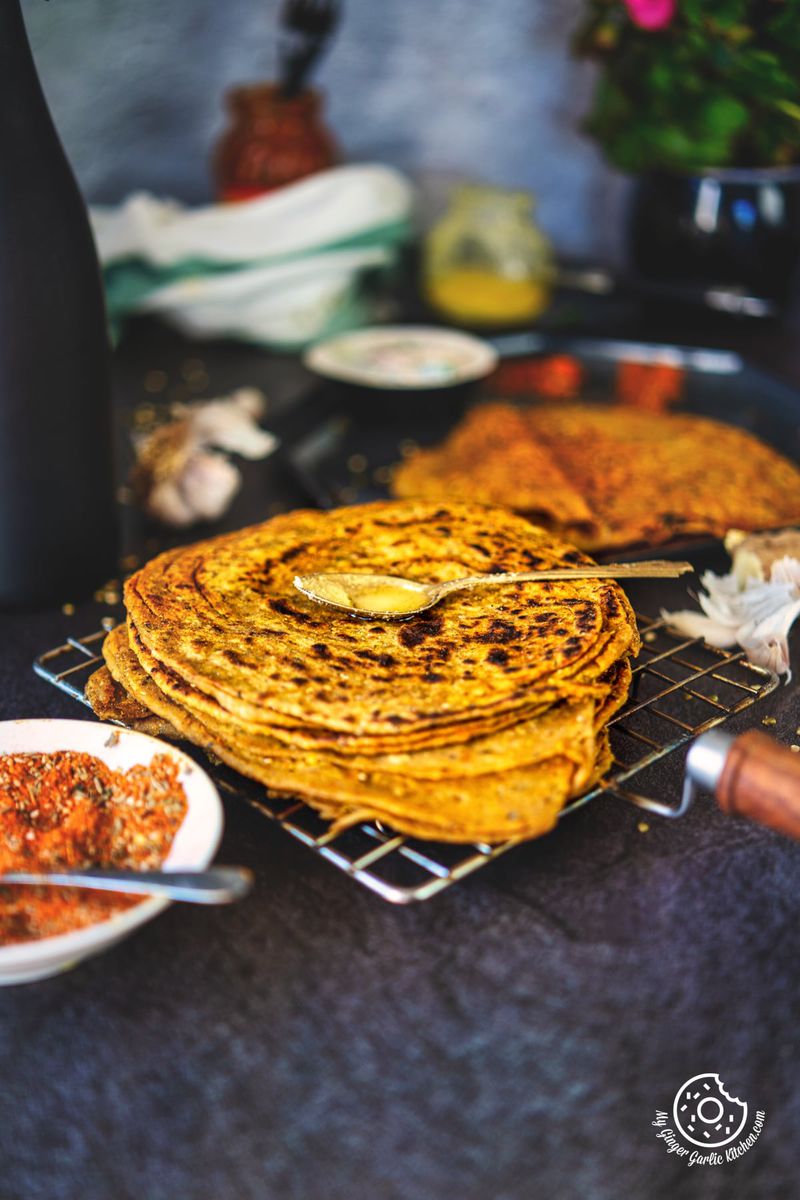 a metal spoon filled with ghee kept on khichdi lachha paratha stacked on a wired rack