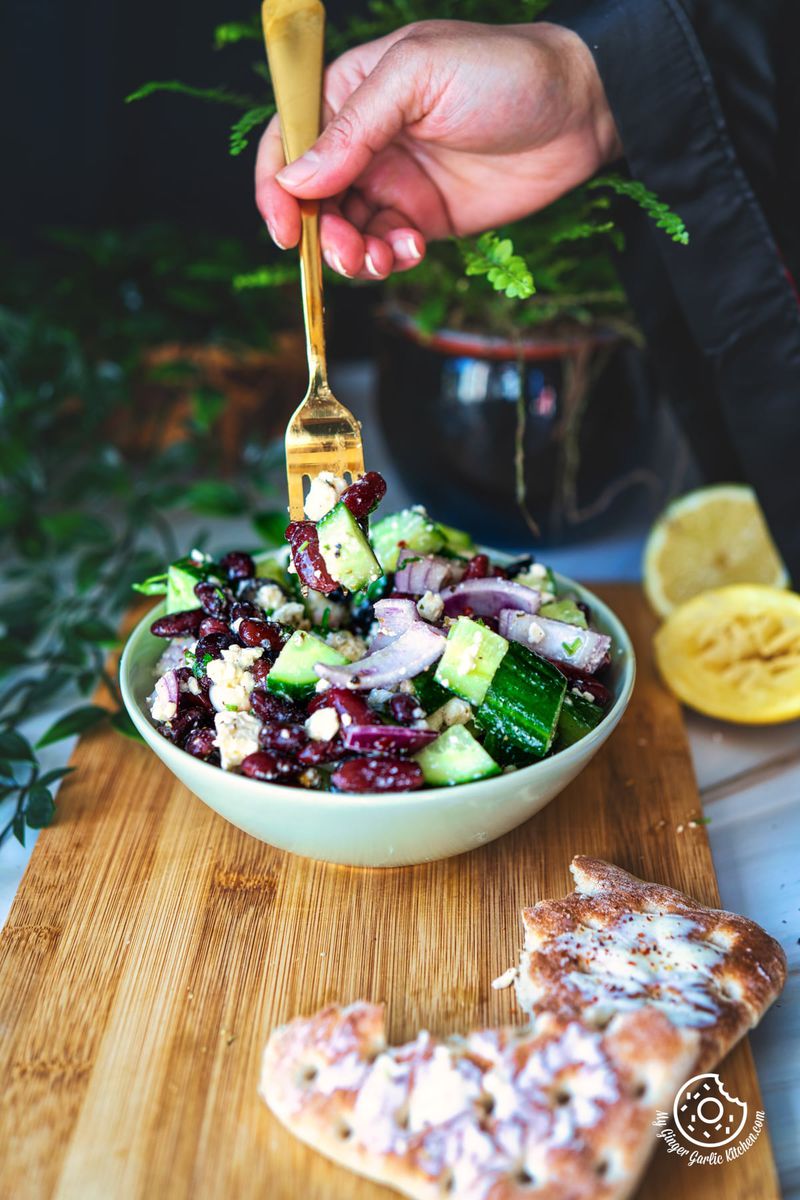 photo of a person is holding a golden fork over a bowl of kidney bean salad on a cutting board