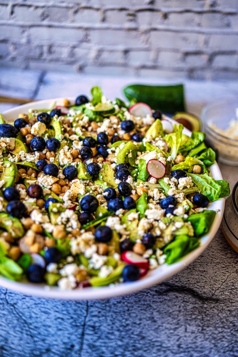 Fresh kiwi chickpea feta salad with avocado, blueberries, cucumber, radishes, and butter lettuce served with lemon mustard dressing.