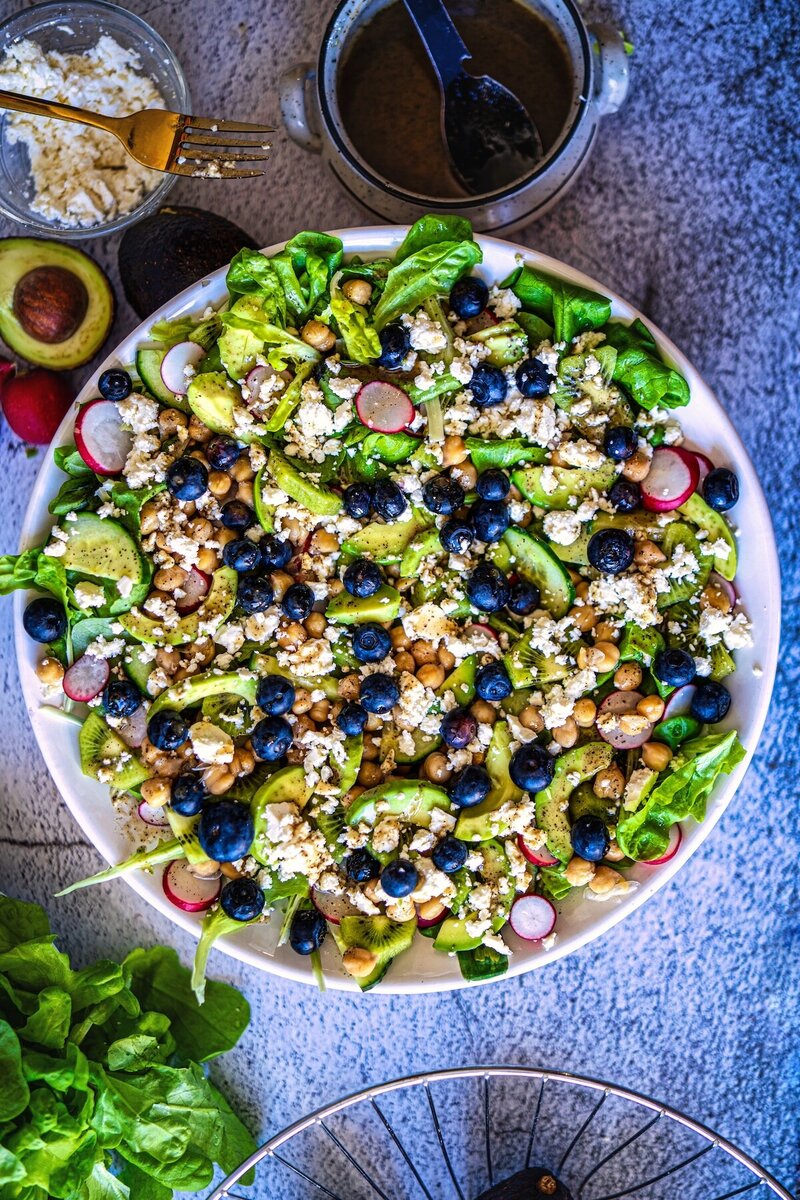 Top view of kiwi chickpea feta salad with avocado, blueberries, cucumber, radishes, feta cheese, and leafy greens.