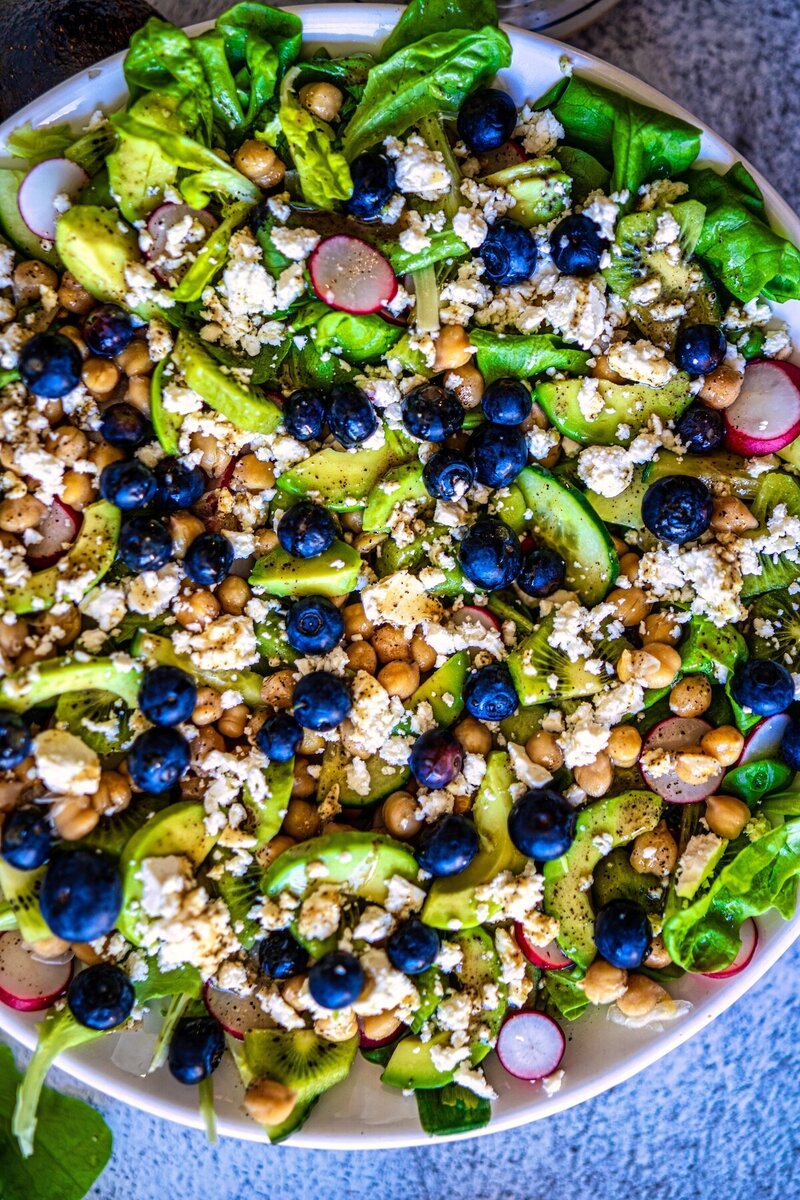 Close-up of healthy kiwi chickpea feta salad with creamy avocado, fresh blueberries, crunchy radishes, and butter lettuce.