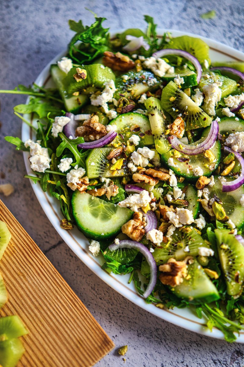 Top-down view of a kiwi and cucumber salad with feta cheese and walnuts on a rustic table.