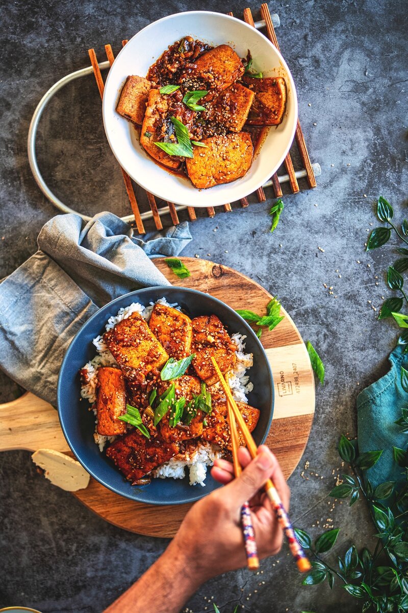 Korean braised tofu aka dubu jorim over steamed rice in blue bowl with sesame seeds and scallions, spicy gochujang garlic sauce, vegan weeknight dinner
