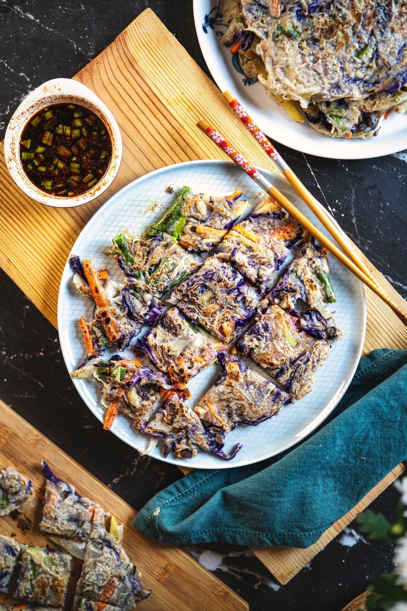 Korean vegetable pancake, sliced and served with soy dipping sauce on a wooden board.