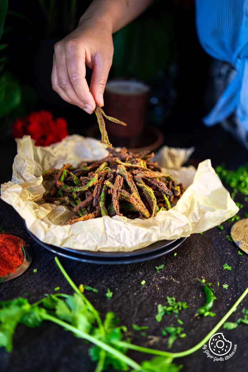 photo of a person is putting a piece of Kurkuri Bhindi on a plate