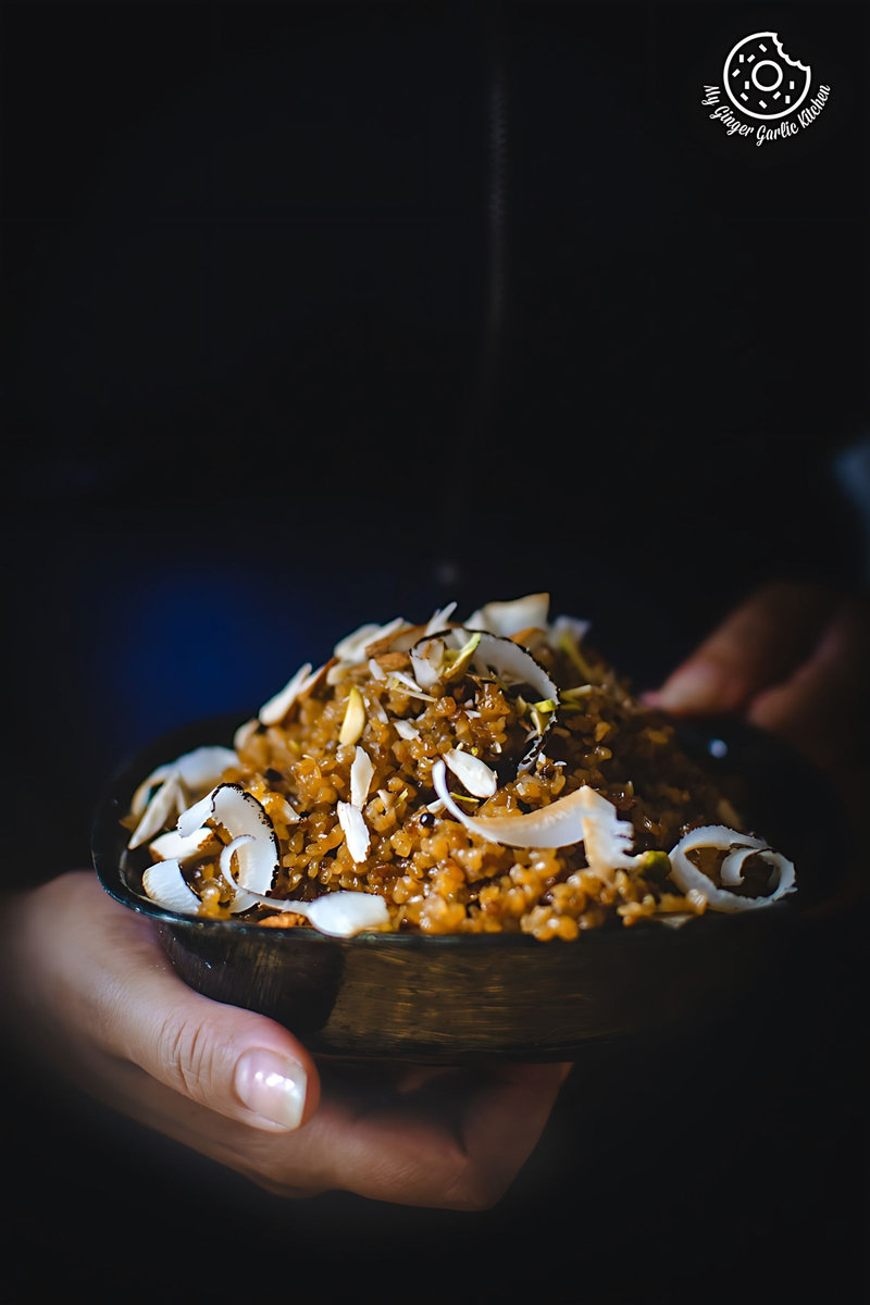 someone holding a bowl of rajasthani lapsi with coconut with nuts and coconut on it