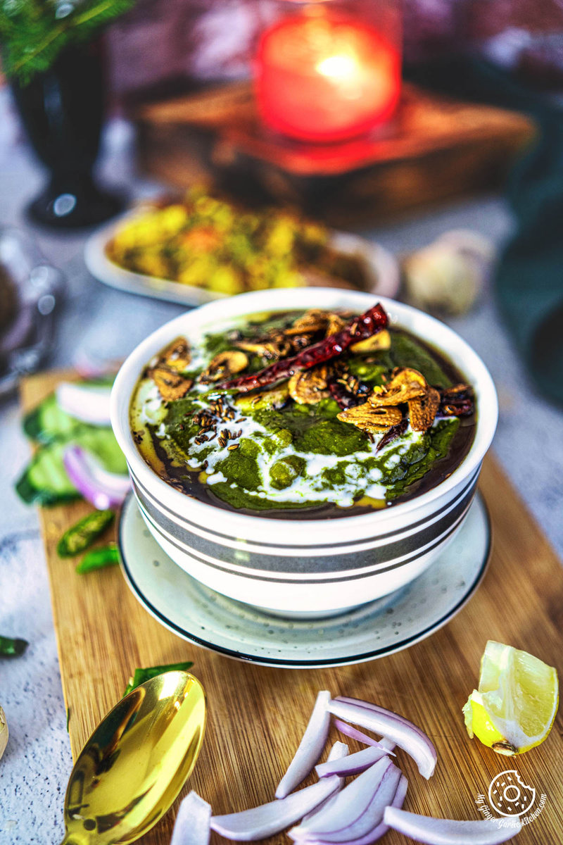 Closeup photo of a bowl of lasooni palak curry, with onions and other ingredients on a cutting board'