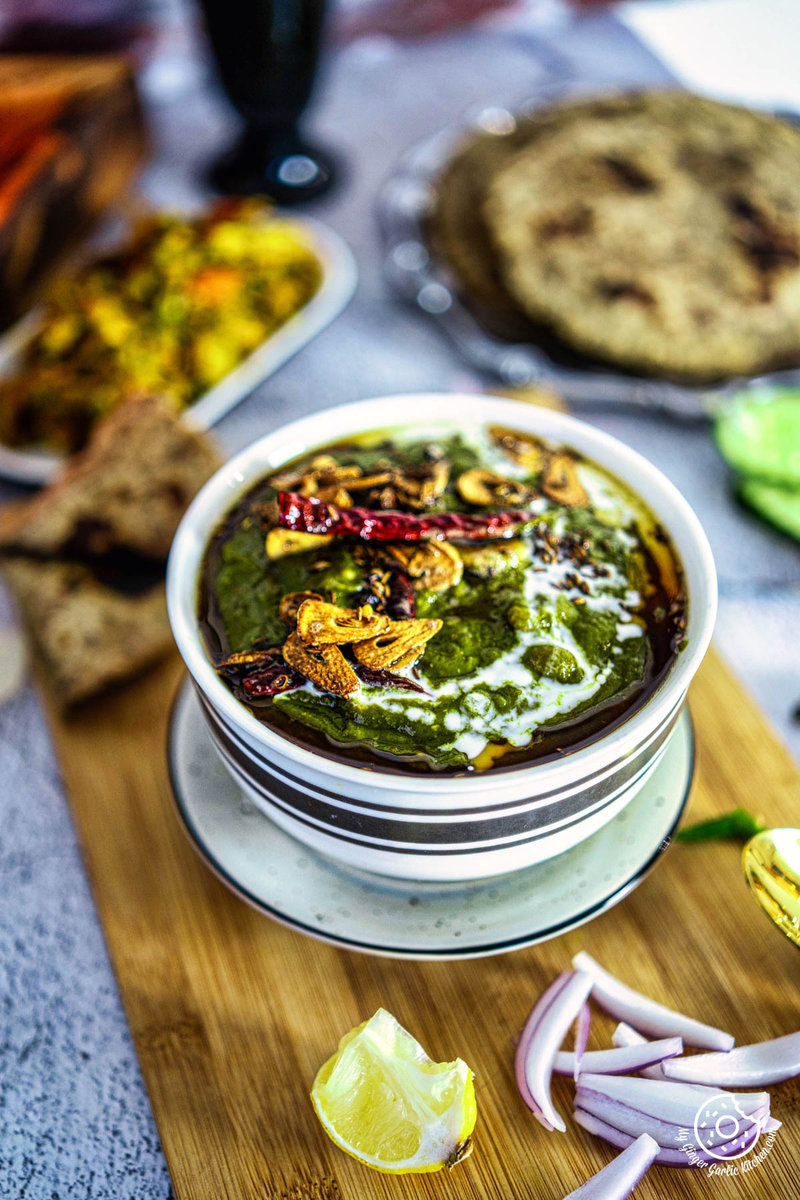 A bowl of lasooni kaju palak or spinach cashew curry, with vegetables and flatbread on a cutting board