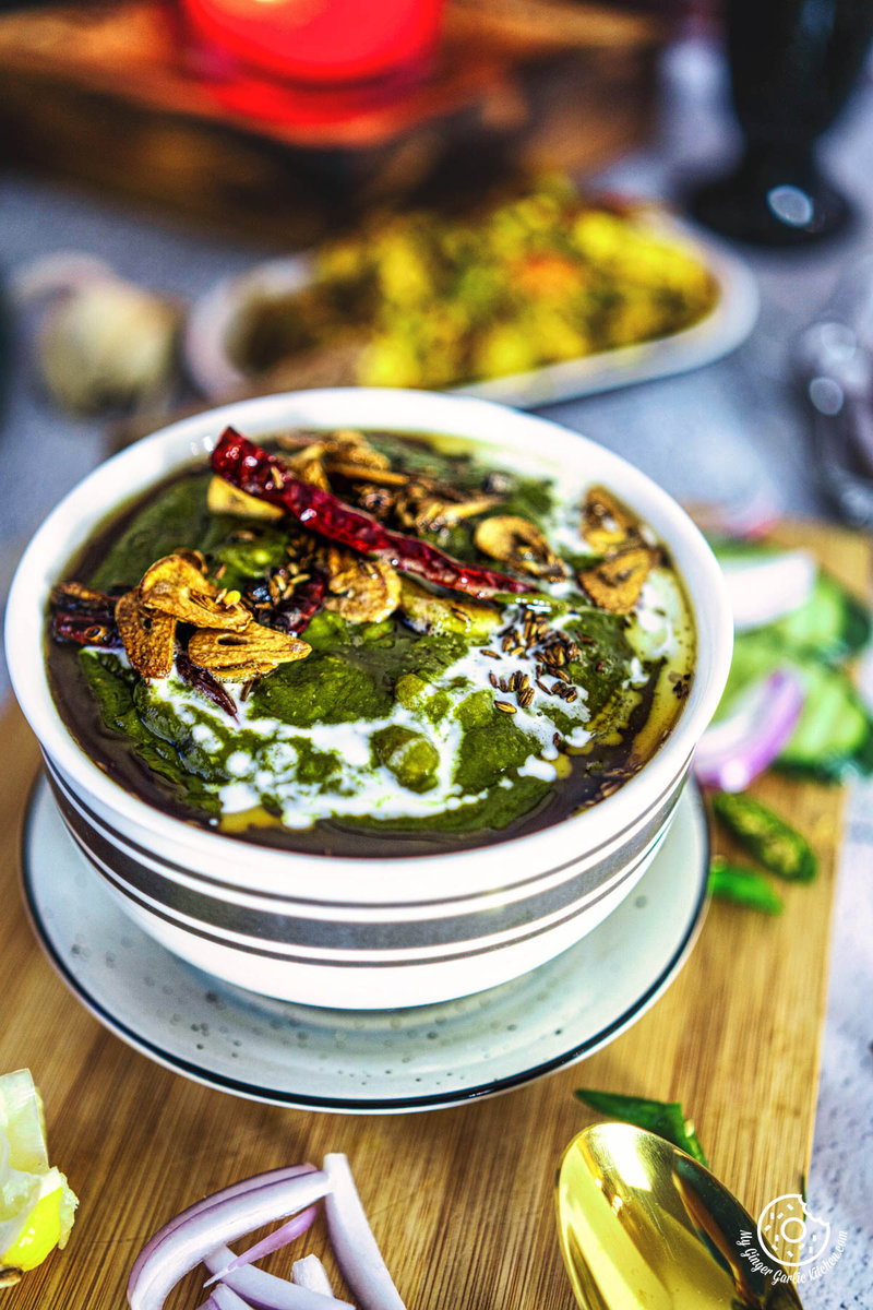 A delicious bowl of lehsuni palak curry on a cutting board with other food