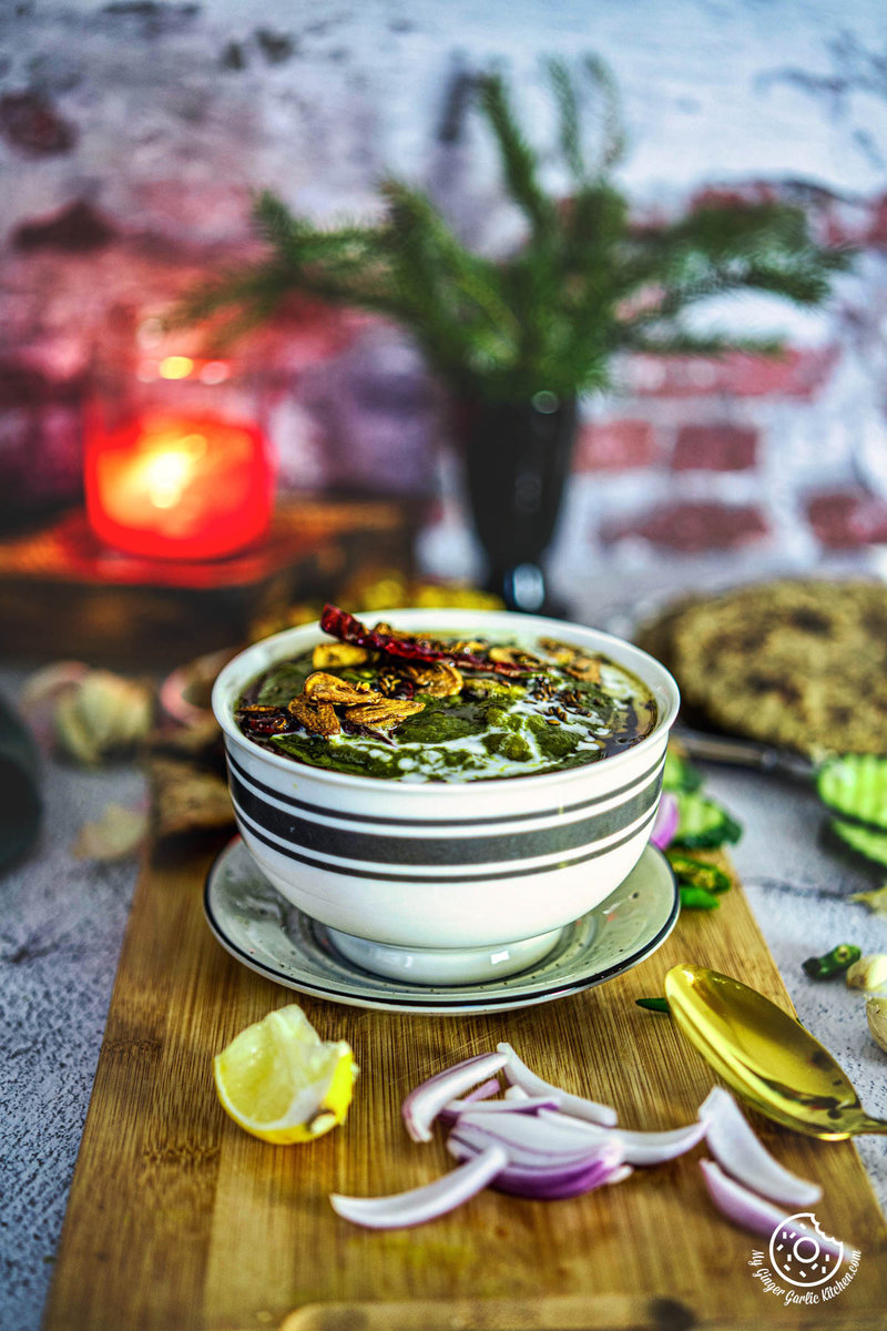 a bowl of lasooni palak with a black stripe on the rim and a candle in the background