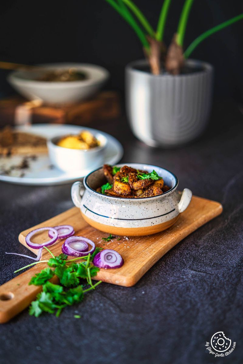 a bowl of leftover french fries aloo masala on a cutting board with a food plate and a plant in the background