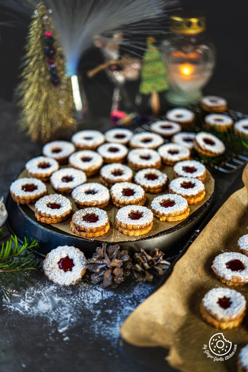 linzer cookies on a gray baking sheet with a golden christmas tree and a candle in the background