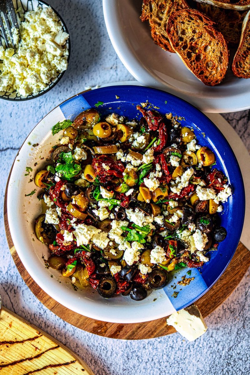 Loaded olive oil bread dip with green and black olives, sun-dried tomatoes, feta, cilantro, and crispy toasted baguette