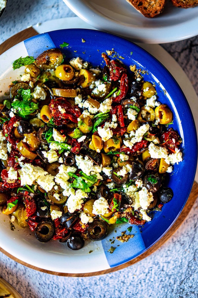 Close-up of loaded olive oil bread dip topped with feta, olives, sun-dried tomatoes, jalapeños, and fresh cilantro