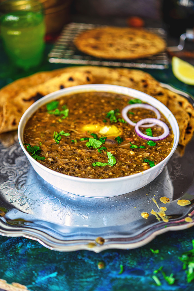Maa Ki Dal served in a white bowl garnished with fresh herbs and onion rings, accompanied by paratha and lemon slices on a decorative silver tray.
