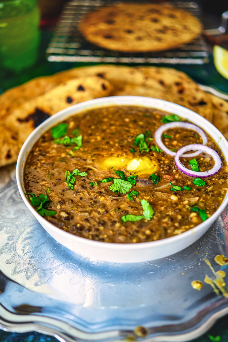 Close-up of Maa Ki Dal in a traditional Indian serving bowl, topped with butter and garnished with cilantro and onion rings, ready to serve.