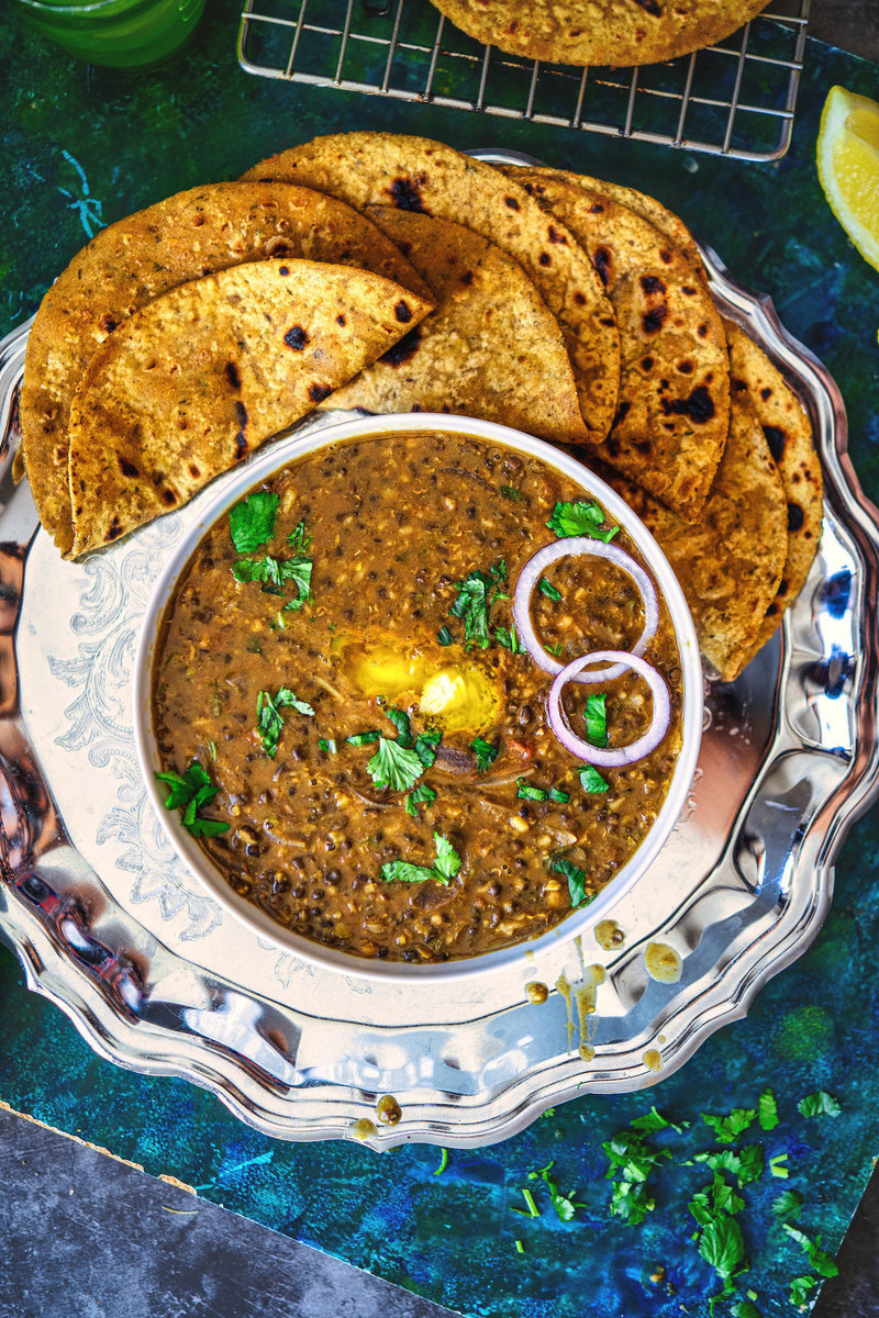 Maa Ki Dal served elegantly in a silver bowl with coriander garnish, alongside charred roti and a rustic metal grill background.