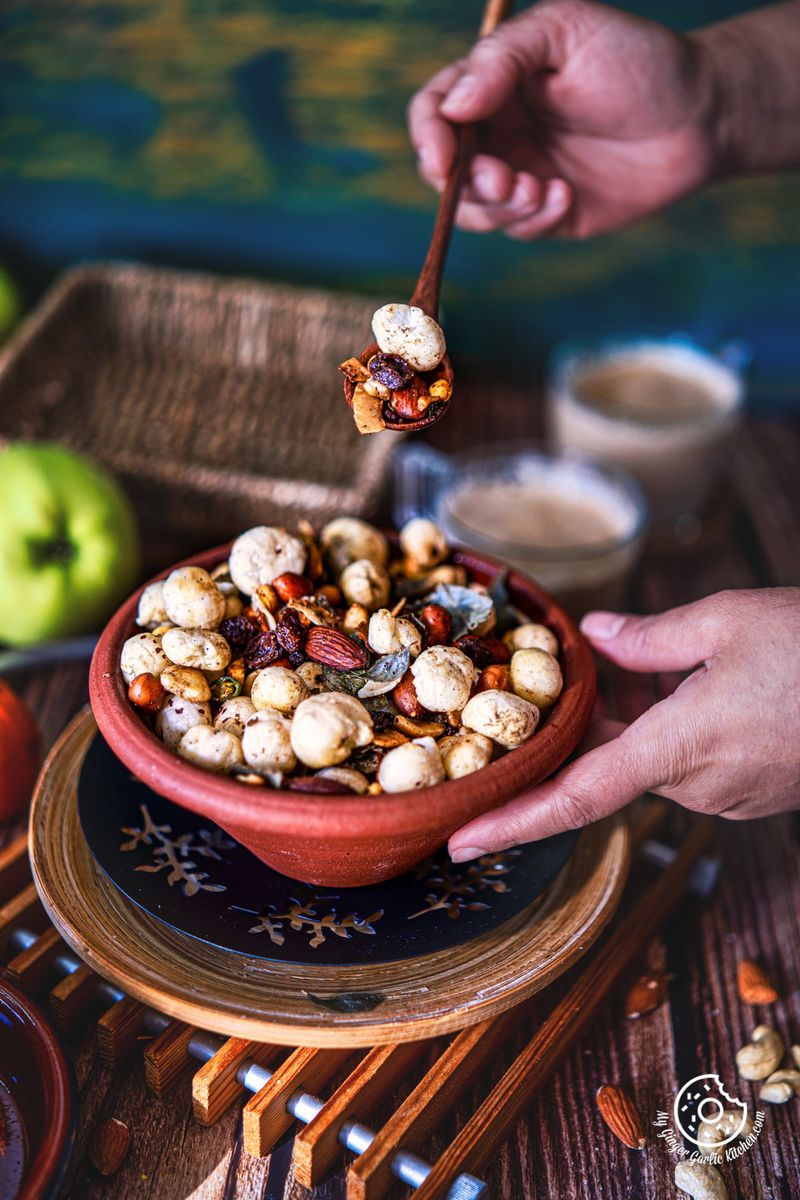 makhana namkeen in a brown earthen bowl and a hand holding namkeen filled wooden spoon over the bowl