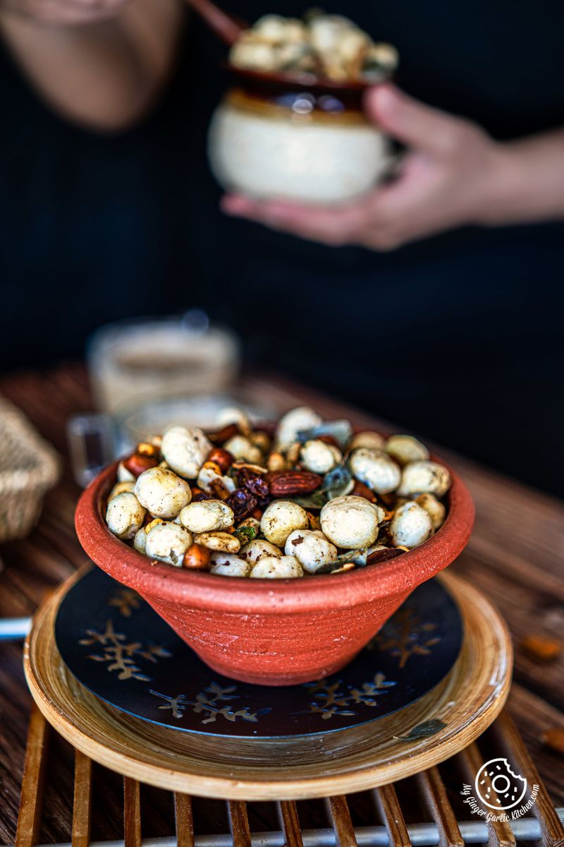 makhana namkeen in a brown earthen bowl and a female holding a white pot in the background