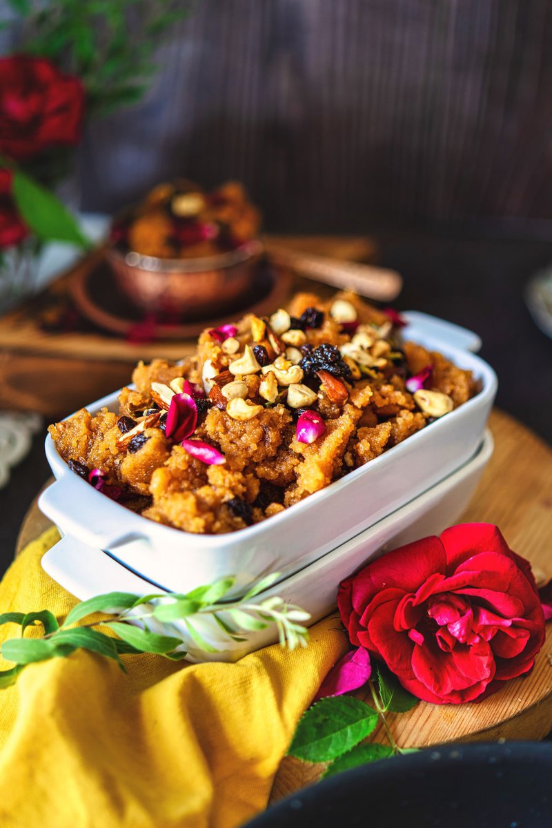 Side-angle shot of makhandi halwa in a white serving dish, adorned with nuts and rose petals, with a red rose and yellow fabric accentuating the scene