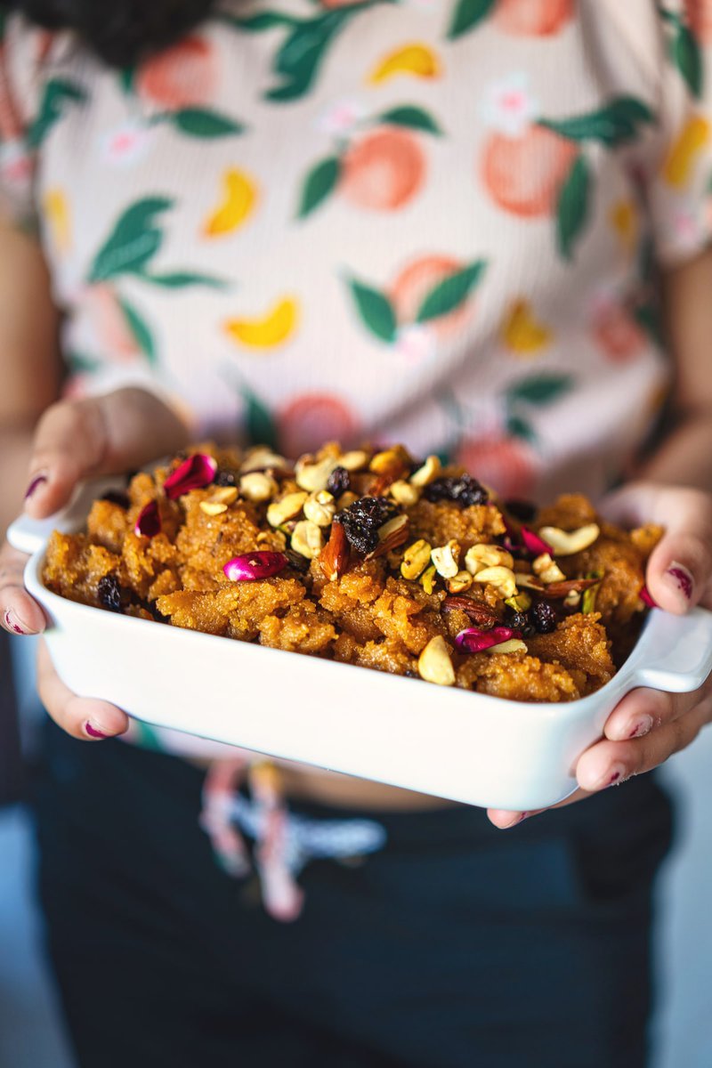 Person holding a dish of makhandi halwa, topped with nuts and rose petals, adding a human touch to the vibrant dessert presentation.