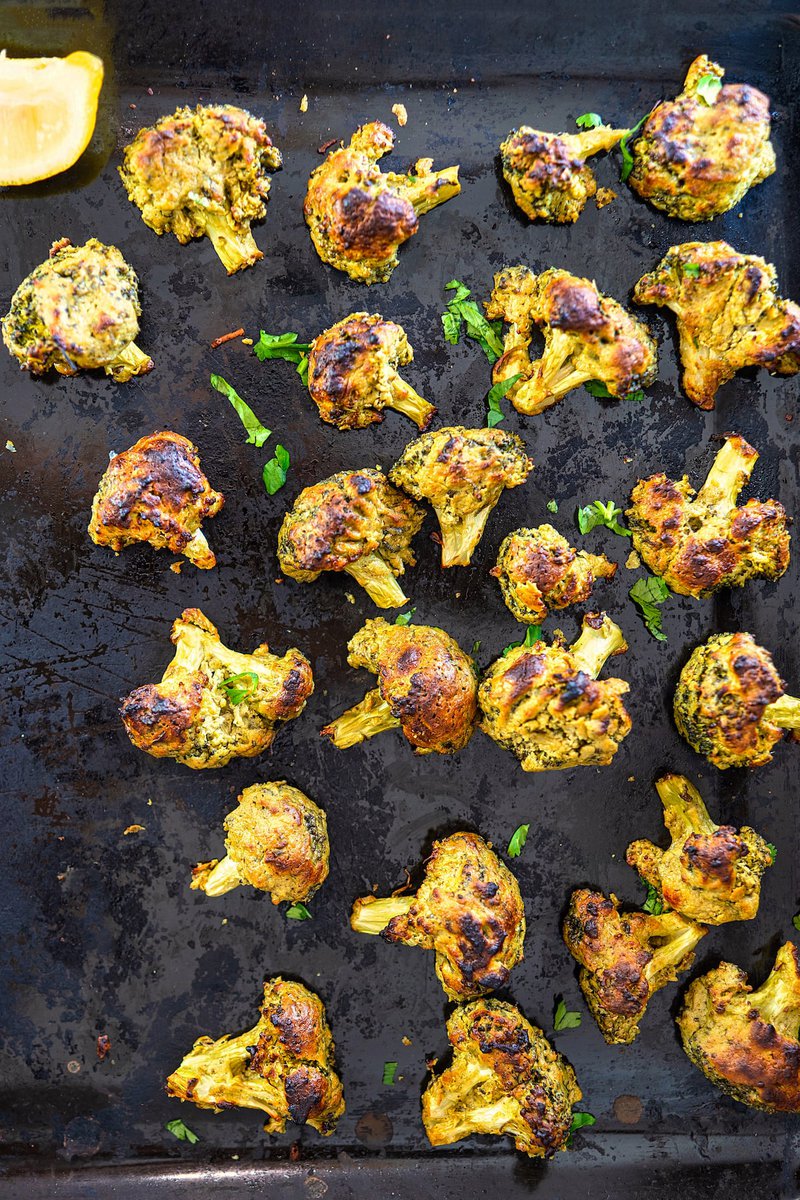 Roasted malai broccoli on a baking tray, garnished with fresh herbs.