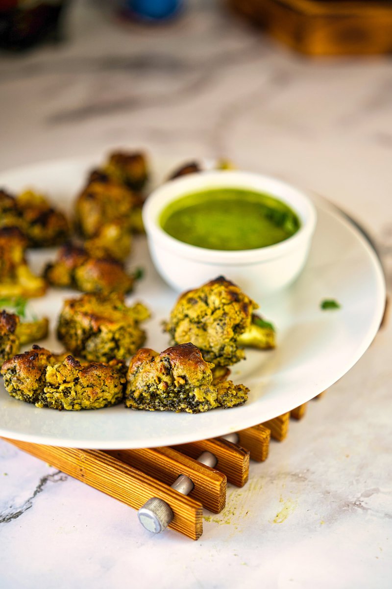 late of malai broccoli served with green chutney on a wooden trivet.