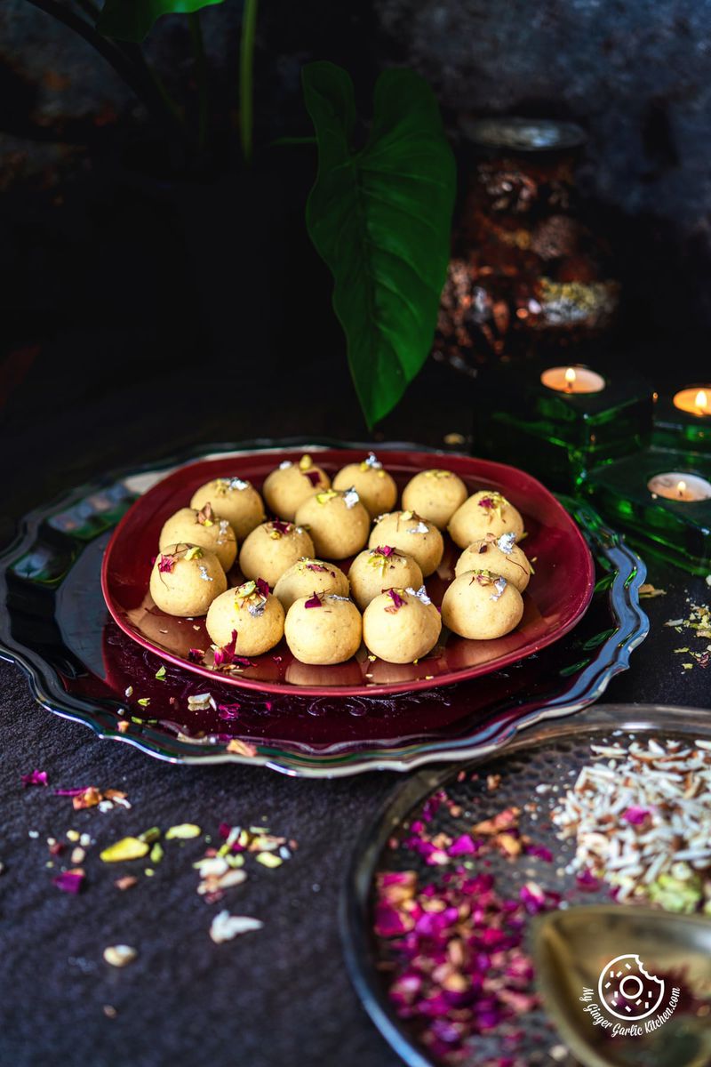17 malai ladoo in a maroon plate with dried rose petals and nuts on the side