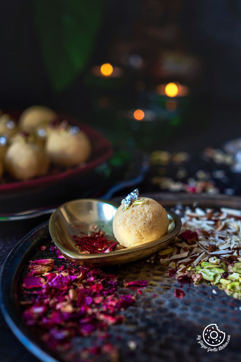 1 malai ladoo decorated with silver leaf in a golden metal plate with some dried rose petals