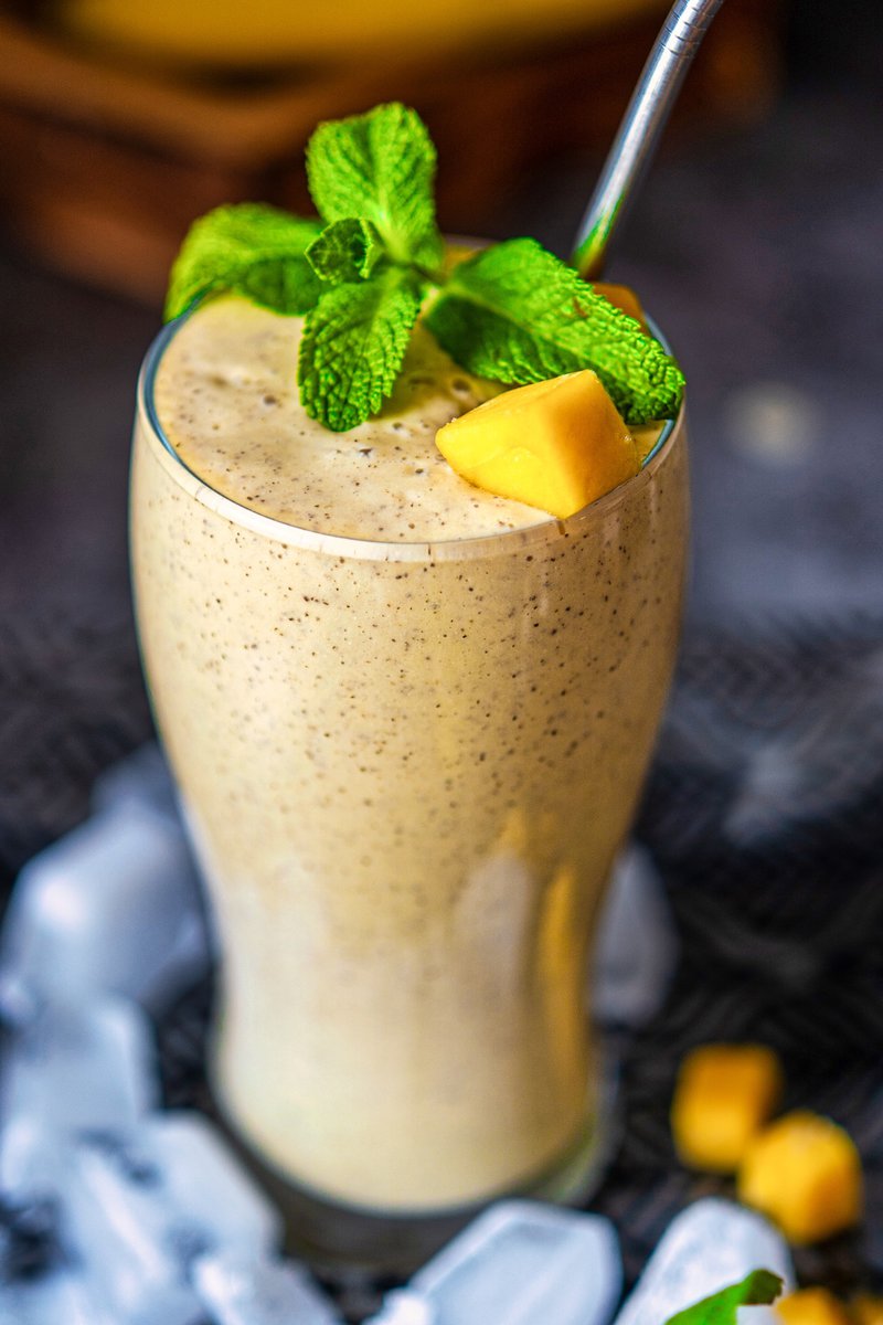 Close-up of a mango banana chia smoothie in a glass, topped with mango pieces and mint, displayed with a metal straw