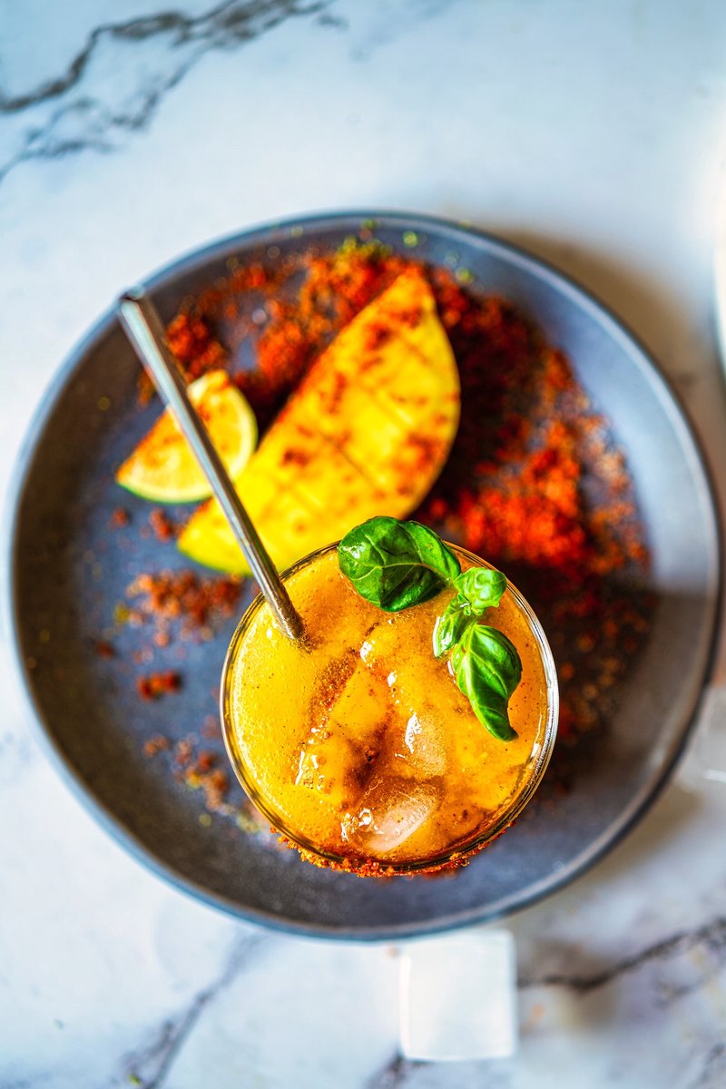 Top view of a refreshing Mango Chili Lime Spritz with basil, ice cubes, and homemade chili-lime seasoning for an easy summer mango mocktail.