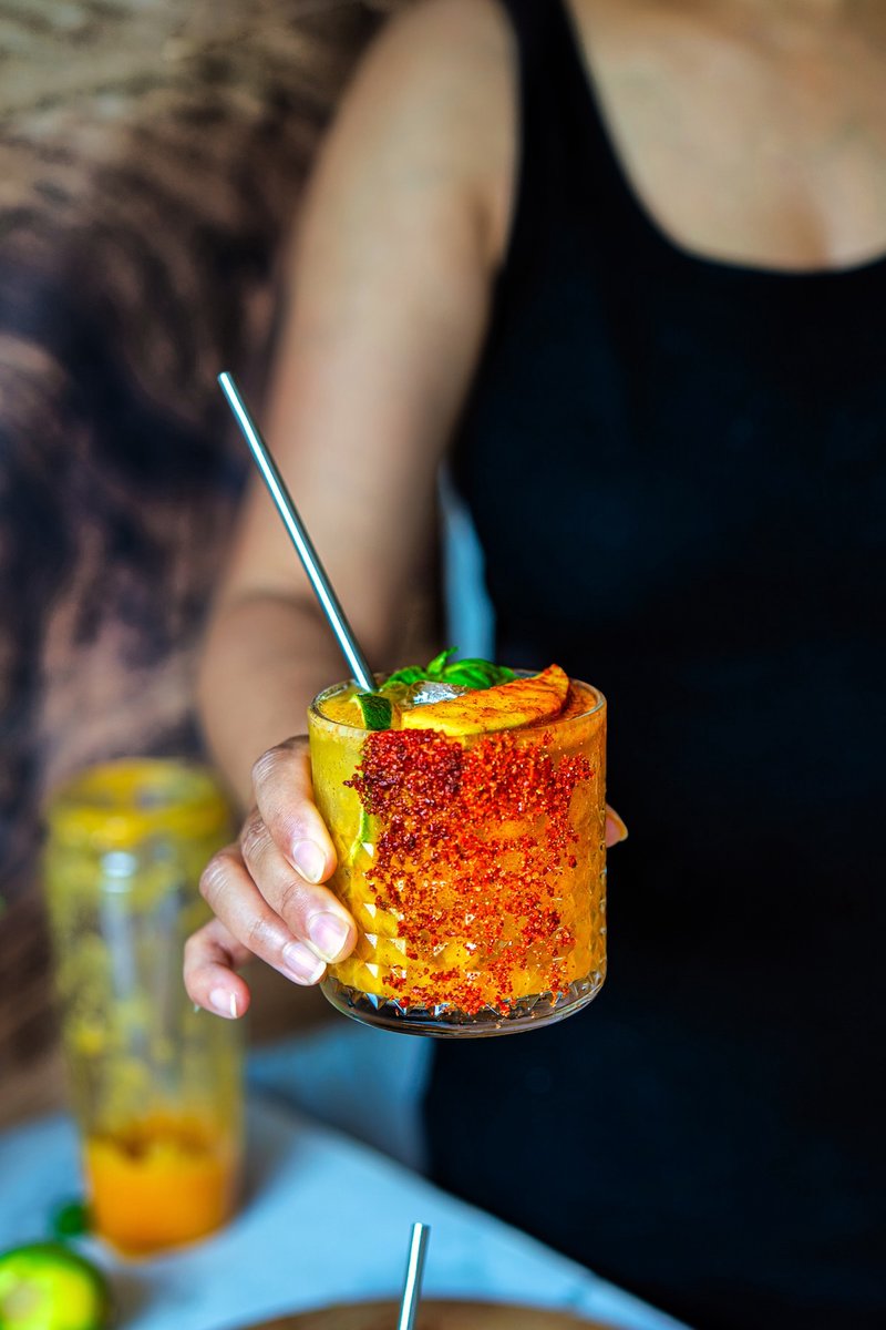 Refreshing Mango Chili Lime Spritz served with a chili-lime coated glass, fresh mango wedge, basil, and sparkling mango drink.
