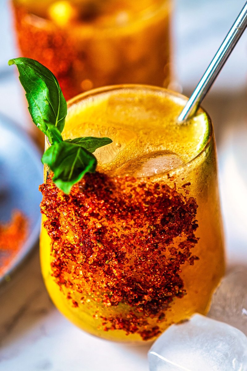 Close-up of a Mango Chili Lime Spritz with chili-lime seasoning, fresh basil, lime slice, ice cubes, and sparkling mango mocktail.
