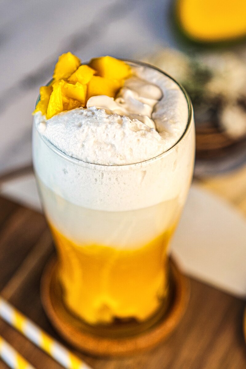 Mango coconut latte close-up with creamy coconut foam topping and fresh mango chunks, vegan layered drink