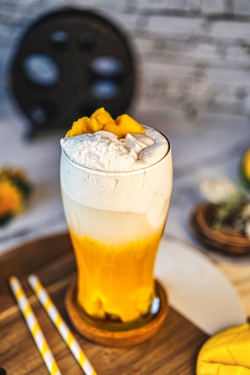 Mango coconut latte in tall glass with layered mango puree coconut milk and coconut cream on wooden board