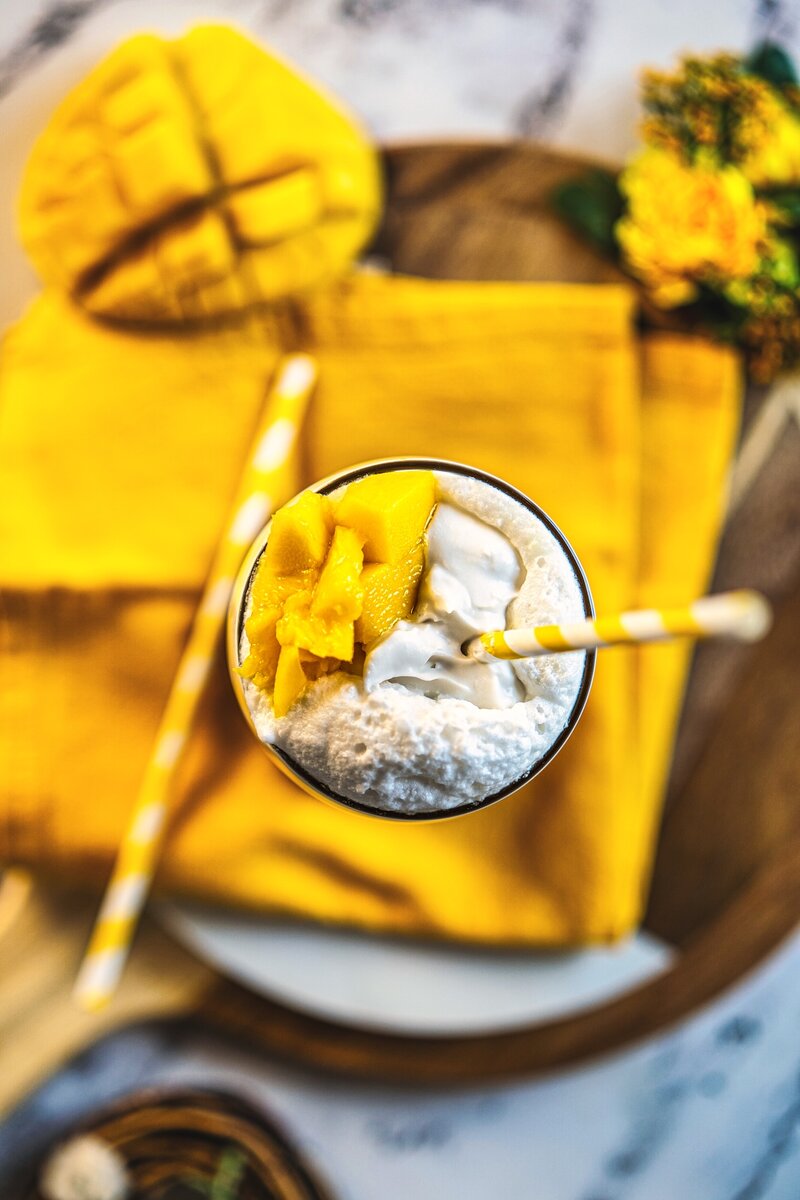 Top view mango coconut latte with coconut cream topping and fresh mango pieces in layered mango drink
