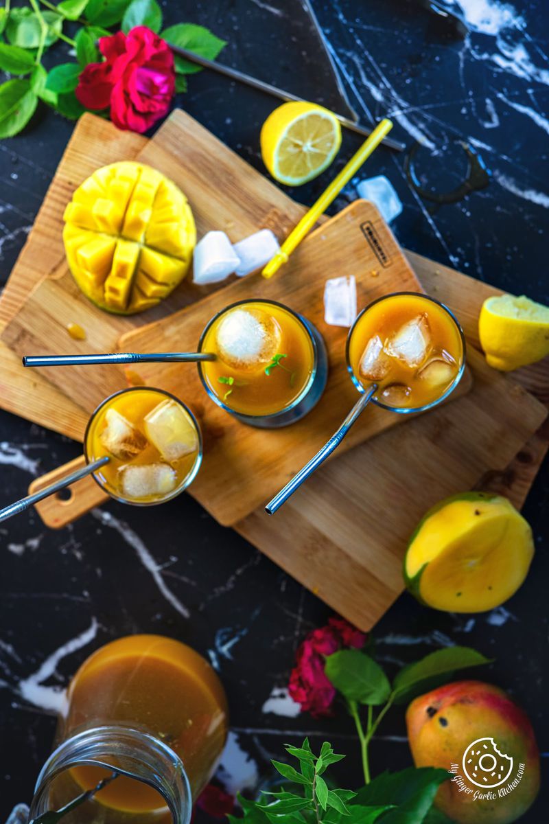 overhead shot of mango iced tea in three glasses with ice cubes and a straws with ice cubes and mango slice on the side