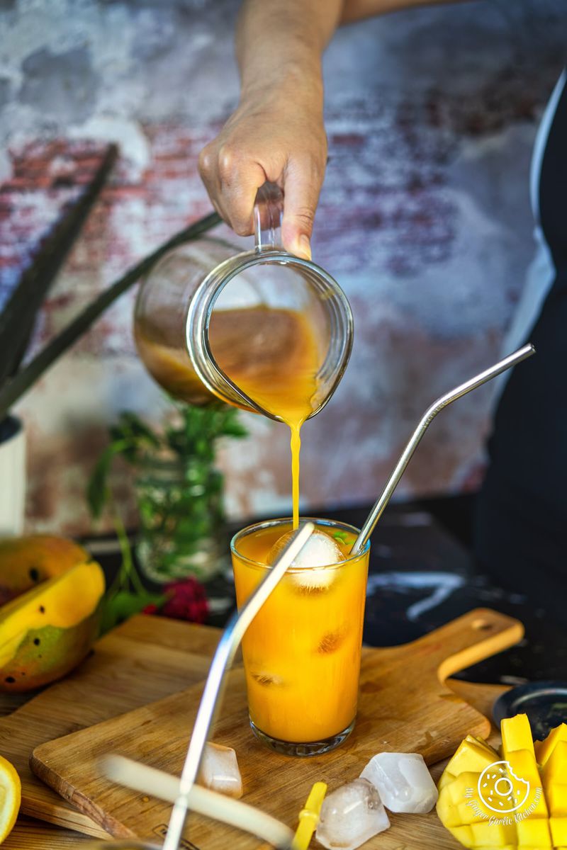 a female pouring mango iced tea from a pitcher into a glass filled with ice