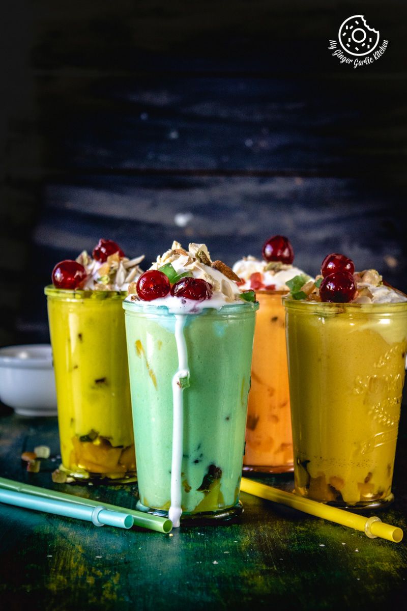 three different colored mango mastani glasses with nuts and cherries