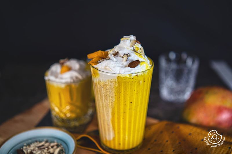 mango milkshake topped with whipped cream and nuts and a small milkshake glass in the background