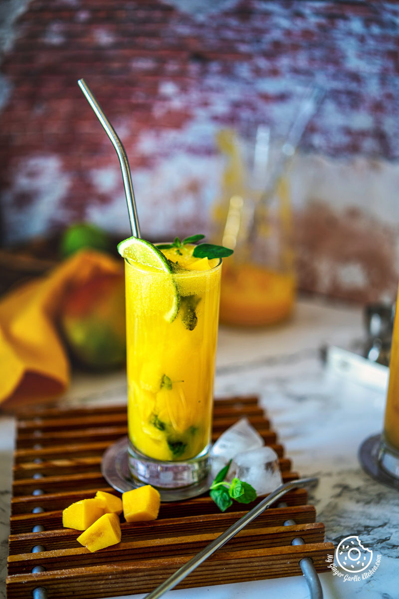 photo of a glass of mango mojito with a straw, mango chunks and a mint leaves