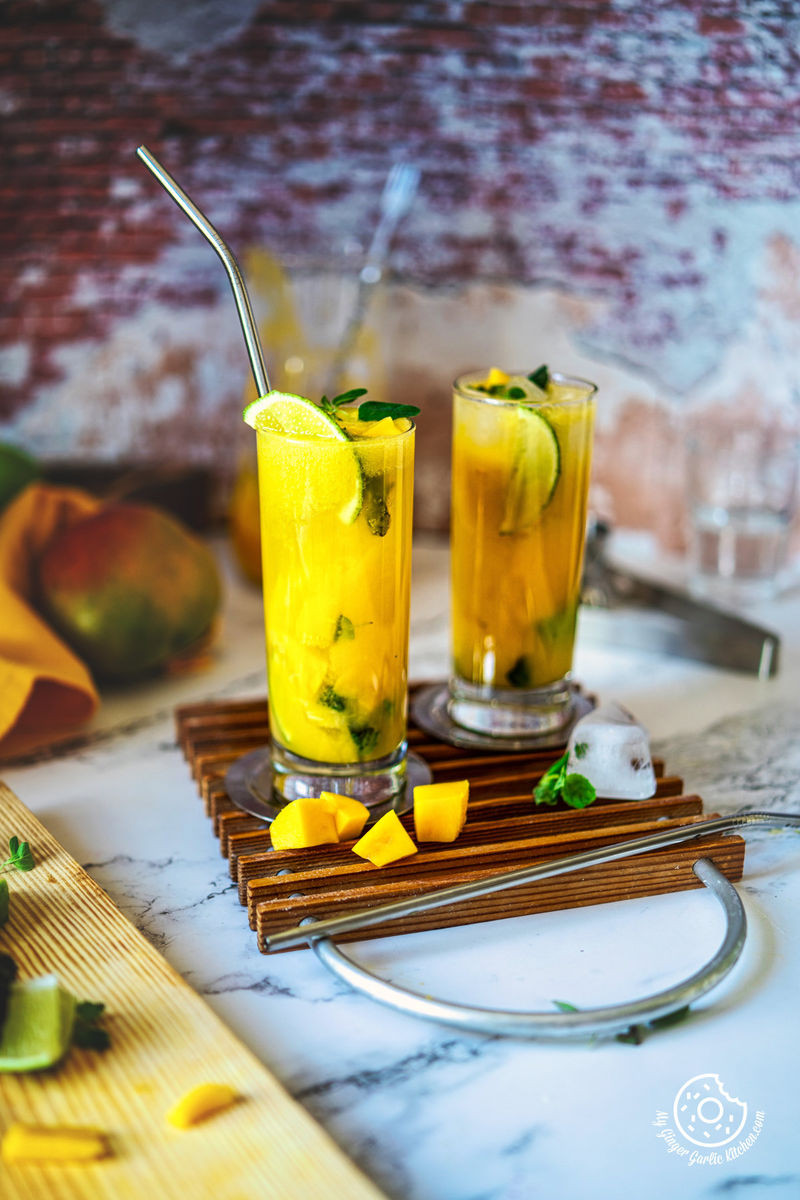 photo of two glasses of fruity drink mango mojito with a straw and ice cube and mango pieces