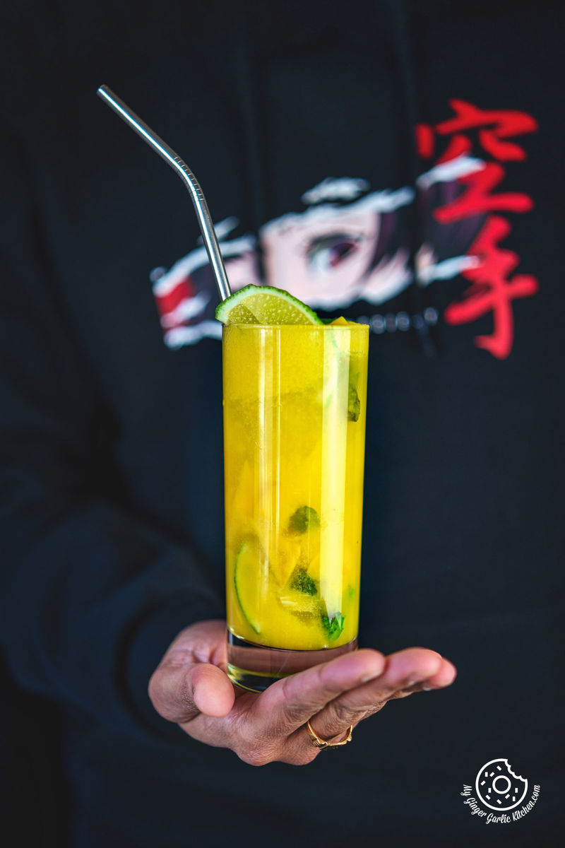 photo of a person holding a glass of a mango mojito drink with a straw