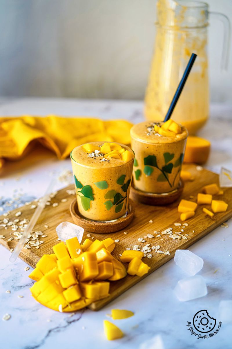 mango oats breakfast smoothie in two glasses with a mango cut slice dice and chunks