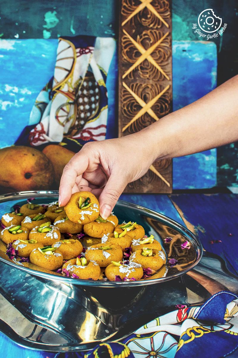 a hand holding mango peda served in a steel tray