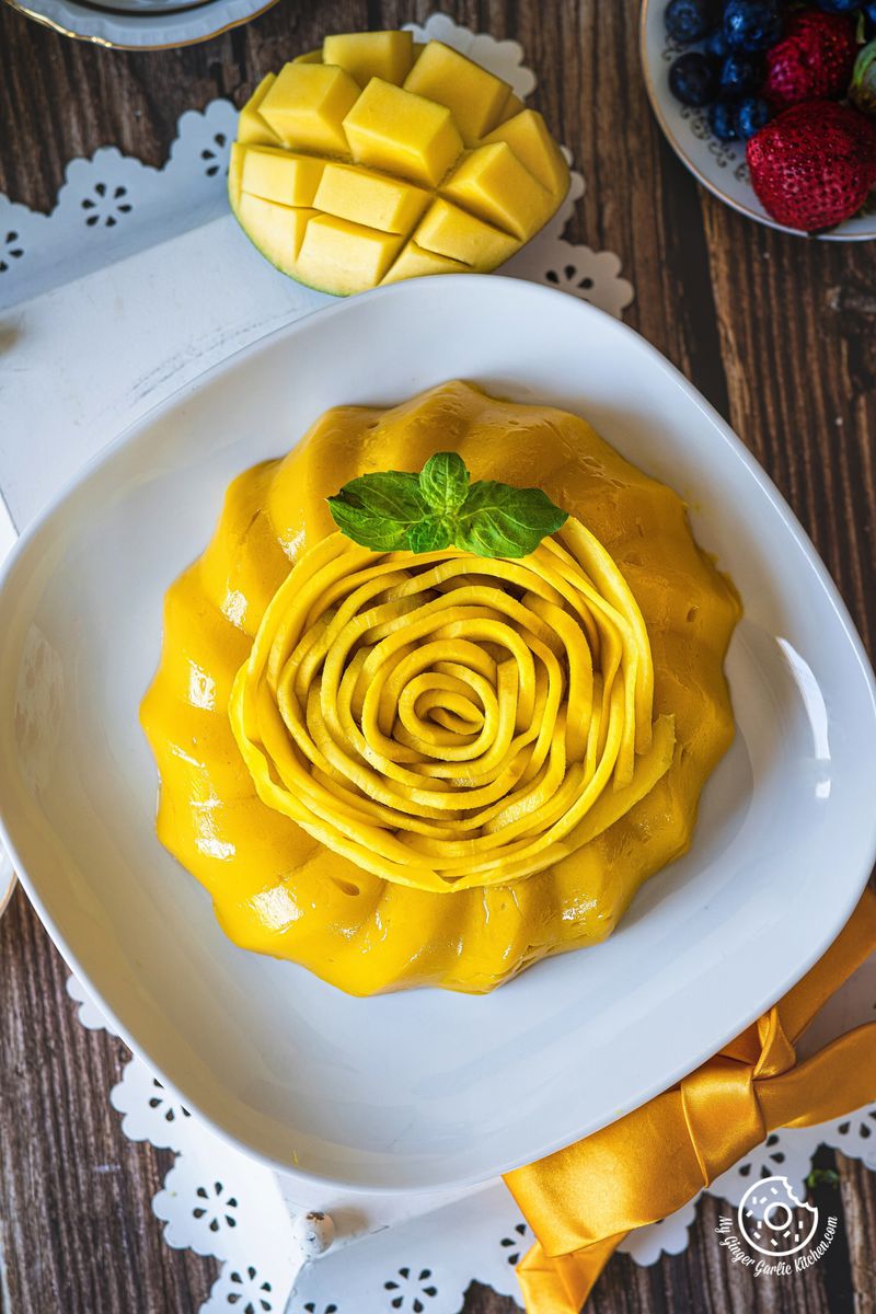 overhead closeup shot of mango pudding decorated with mango rose kept in a white plate