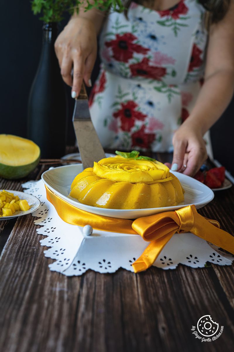 a female is holding a cake lifting spatula with one hand and holding mango pudding plate with the other hand
